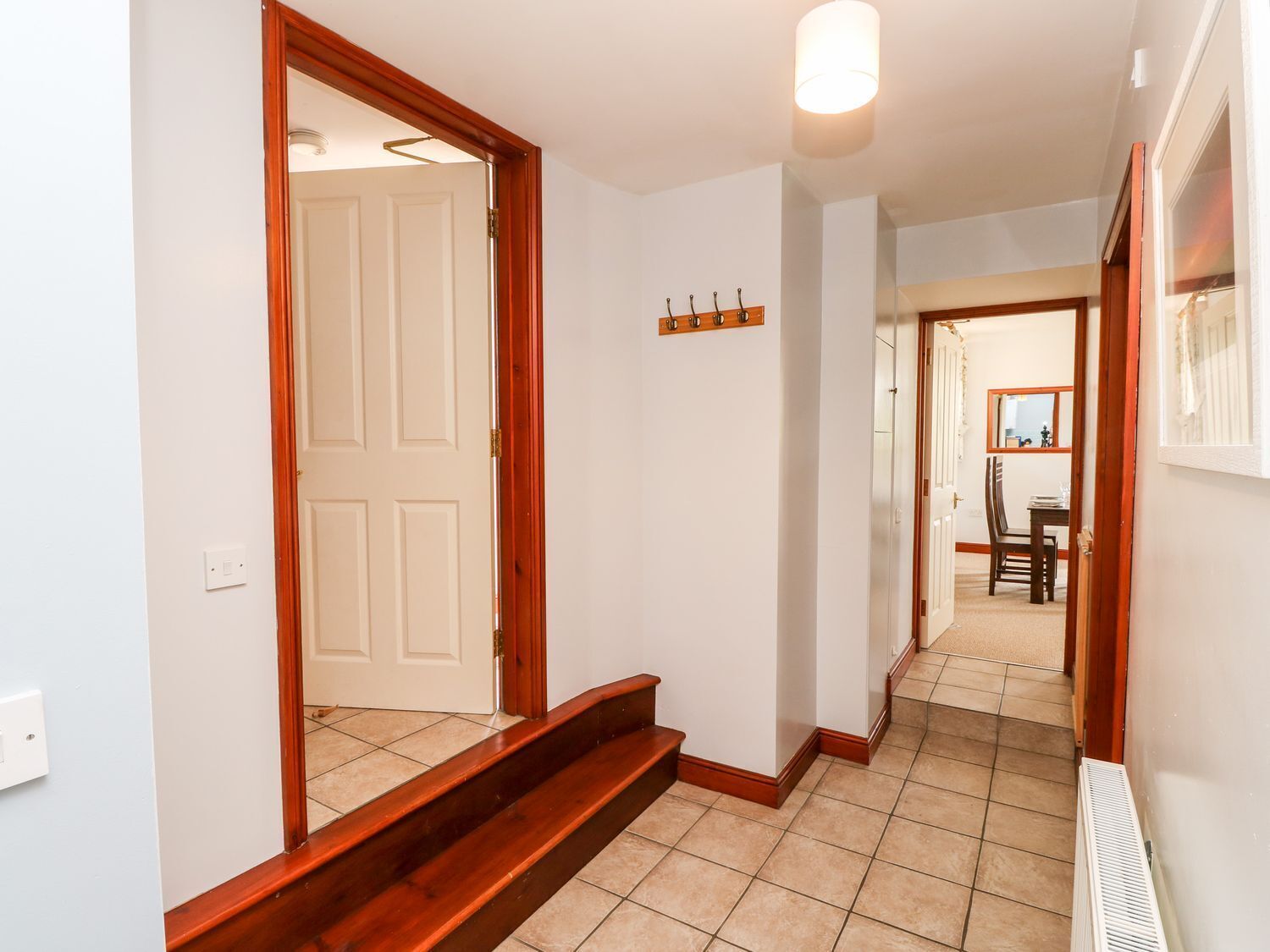 A hallway with a wooden staircase, a white door, and a dining area in the background.