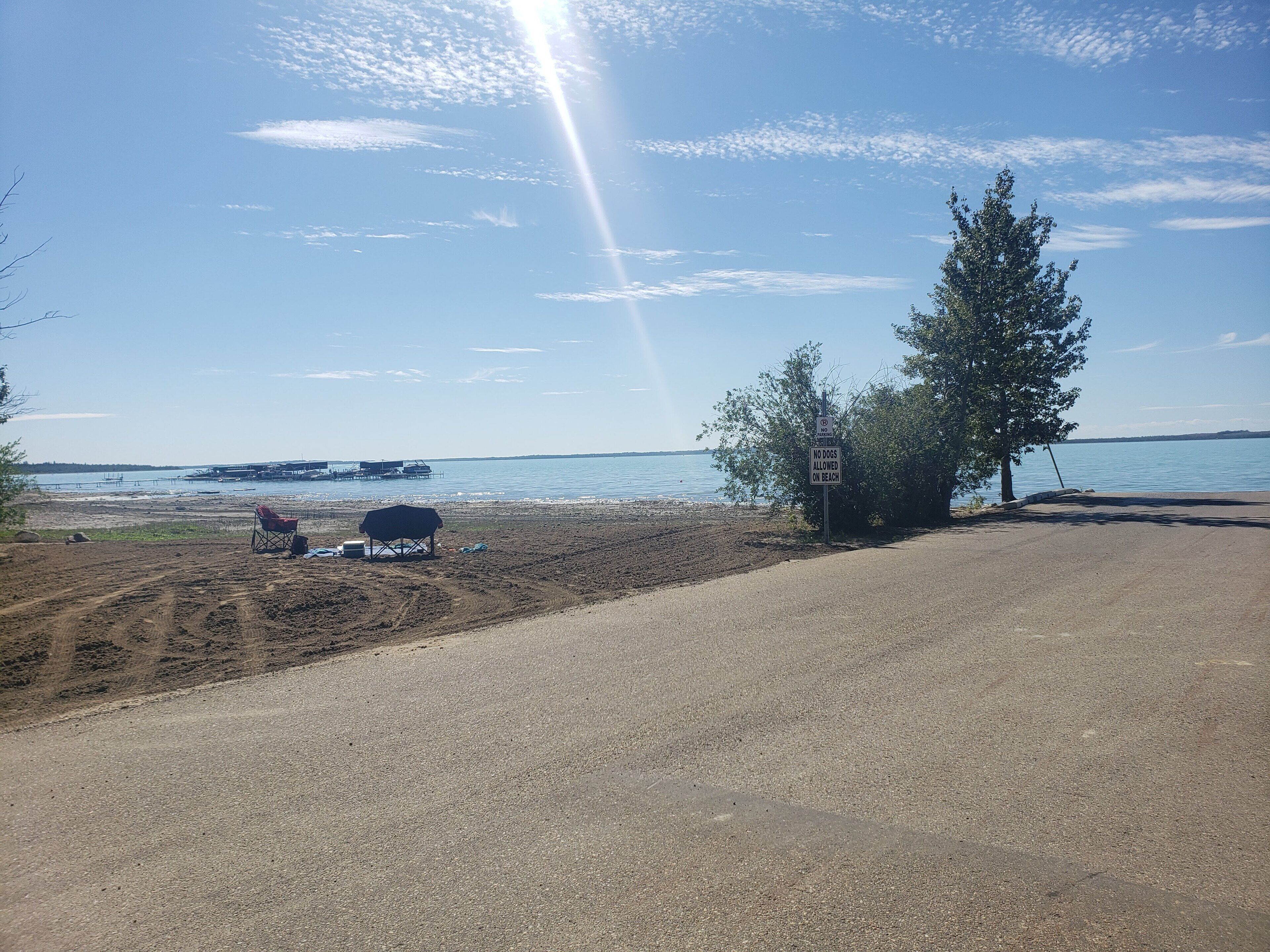 A beach with a no dogs allowed sign, a covered area with a chair and a cooler, and a clear view of the water.
