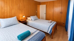Een kamer met twee bedden, houten wanden, een nachtkastje met een lamp en een deur.