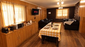 Une cuisine chaleureuse avec une table à manger pour quatre personnes, un téléviseur à écran plat fixé au mur et des meubles de rangement en bois.