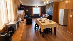 Een knus woongedeelte met een kitchenette, een eethoek met geruit tafelkleed, een bank en een aan de muur bevestigde televisie.