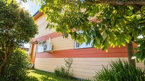 Een huis met een rode en beige gevel, een airconditioning op de zijkant en een verzorgde tuin met diverse planten.