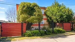 Una propiedad residencial con patio cercado, una reja roja y una casa de fachada roja y beige.