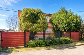 Una propiedad residencial con patio cercado, una reja roja y una casa de fachada roja y beige.
