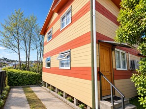 Een meerlaags huis met een rode en gele gevel, een houten deur en een klein voortuintje met treden.