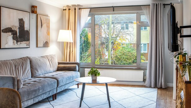 A modern living room with a grey sofa, a round coffee table, and a large window with curtains. - 4 bedroom accommodation in Salisbury, near Dorset (Salisbury, near Dorset)