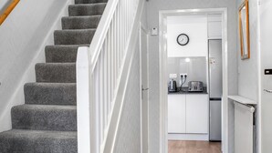 A staircase with carpeted steps and white railings leading to a kitchen area with white cabinets, a clock, and a radiator. - 4 bedroom accommodation in Salisbury, near Dorset (Salisbury, near Dorset)