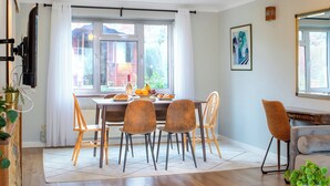 A dining area with a table set for four, chairs, a window with curtains, and a plant on the floor. - 4 bedroom accommodation in Salisbury, near Dorset (Salisbury, near Dorset)