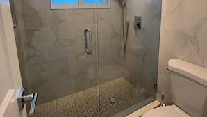 Un baño moderno con ducha envuelta en vidrio, un inodoro y una pequeña ventana sobre la ducha.