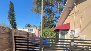 Una entrada cerrada con un portón metálico, una valla de madera y un camino de concreto que lleva a un edificio con toldo rojo.
