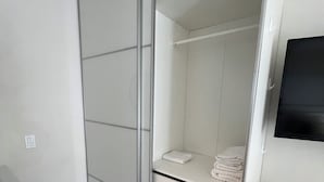 Un dormitorio moderno con una puerta corredera para el armario, una mesita de noche, un televisor montado en la pared y suelo de madera.