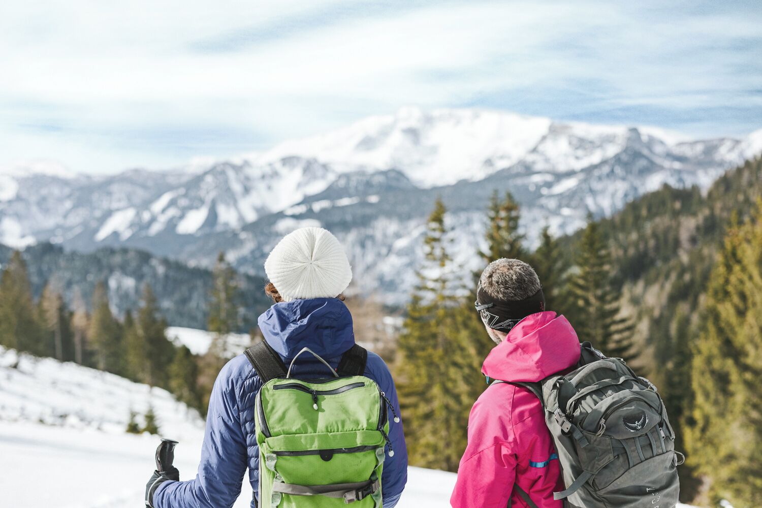 Due persone con zaino su una montagna innevata, con vista su montagne ricoperte di neve.