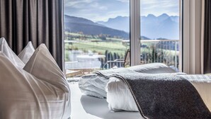 A hotel room with a bed, a view of mountains, and a balcony with outdoor furniture. - Landhotel das Stocker (Vorderstoder)
