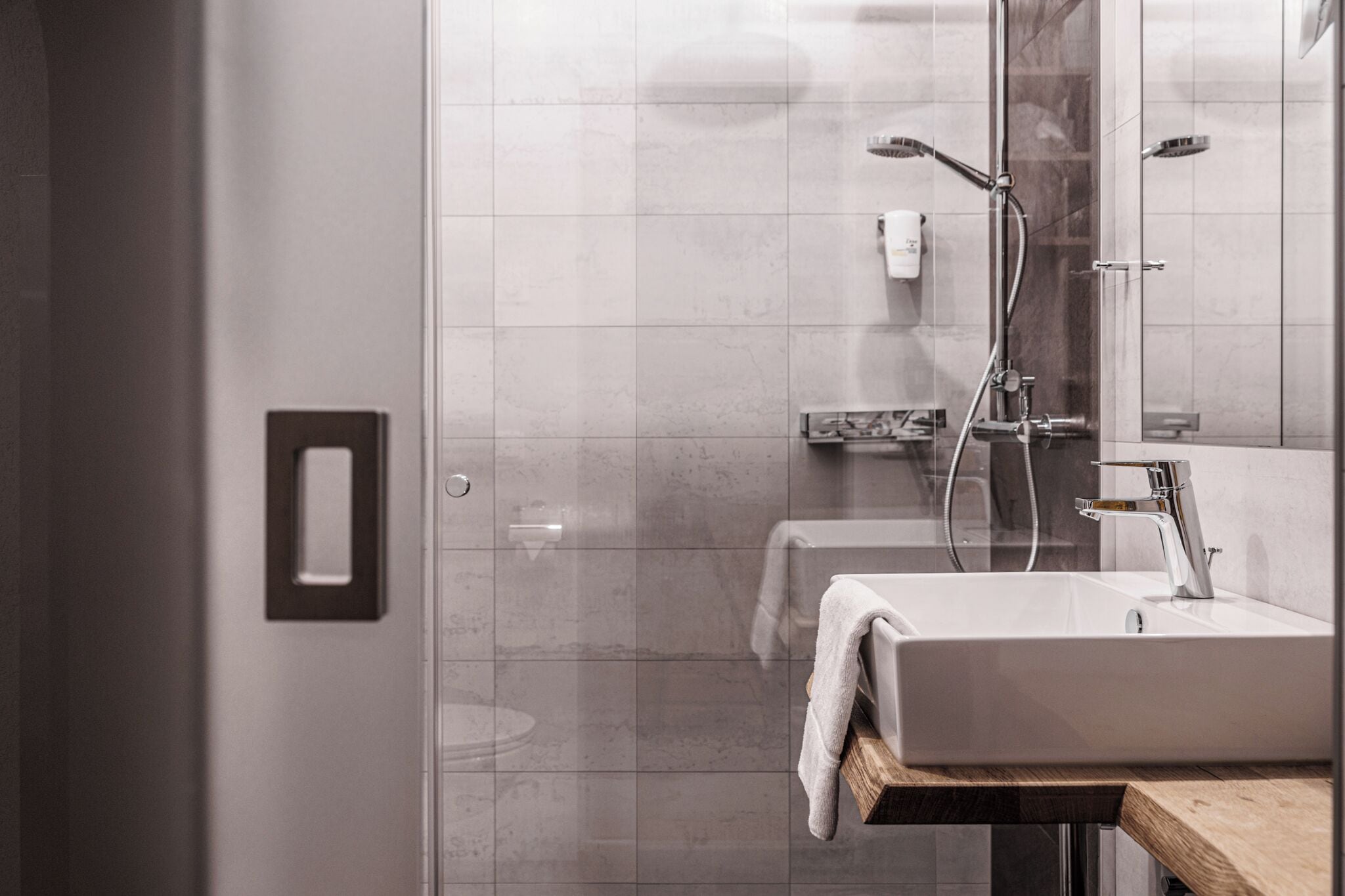 A modern bathroom with a glass shower enclosure, a white sink, and a wooden countertop.