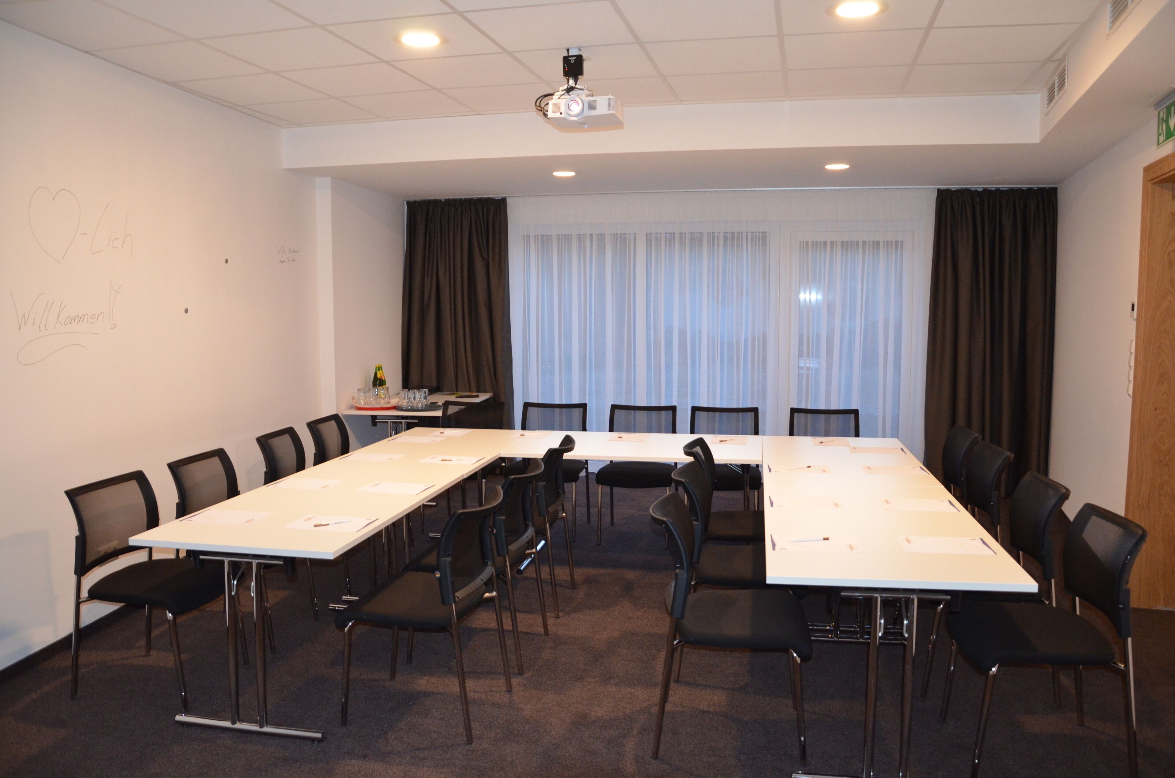 A conference room with a long table, chairs, a projector, and a whiteboard with some writing.