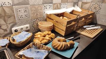 En køkkenbord med forskellige bagværk, blandt andet croissanter og en bundtkage, kurve og en trækasse til brød.