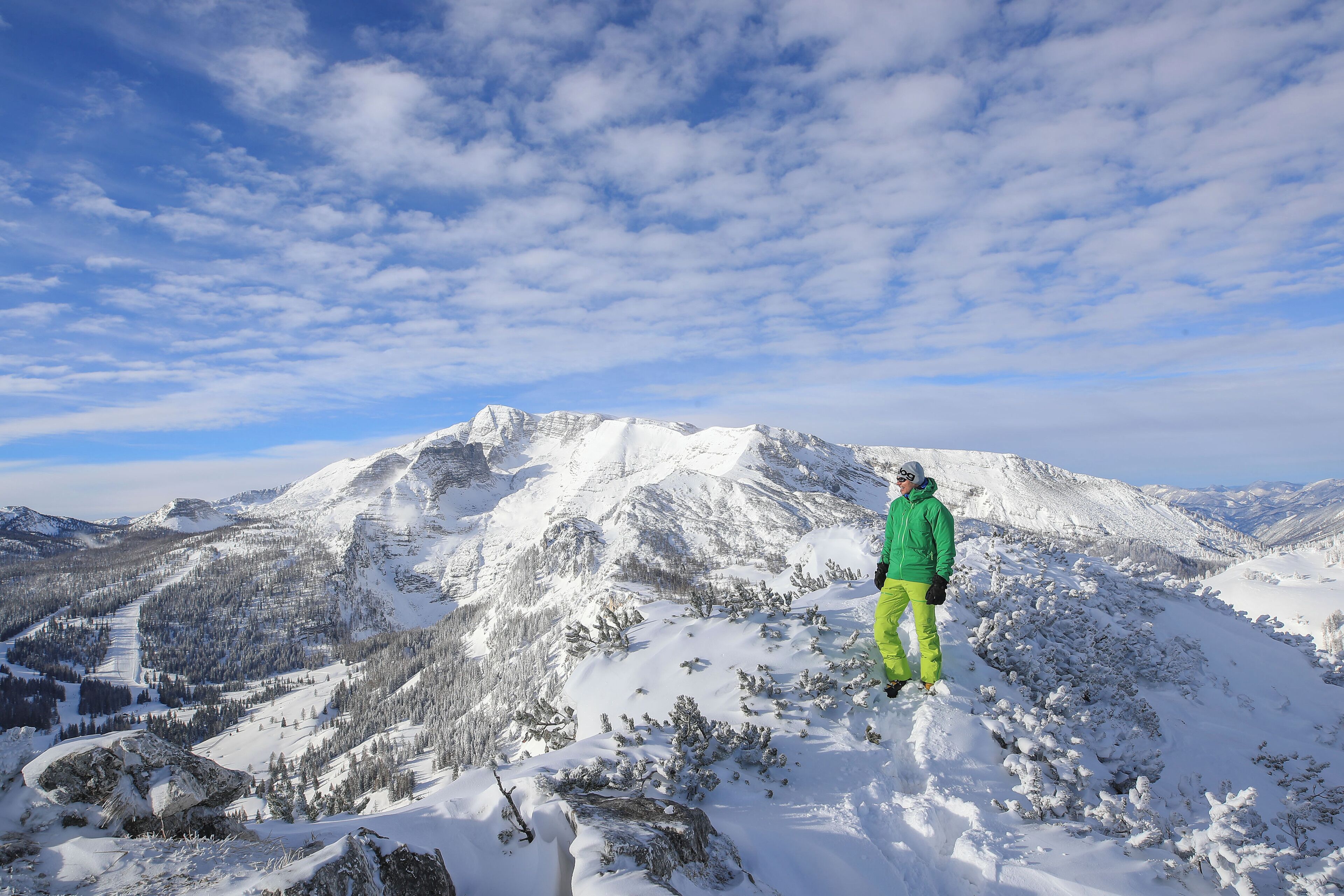 Una persona de pie sobre una montaña nevada, con vistas a otras montañas cubiertas de nieve al fondo.