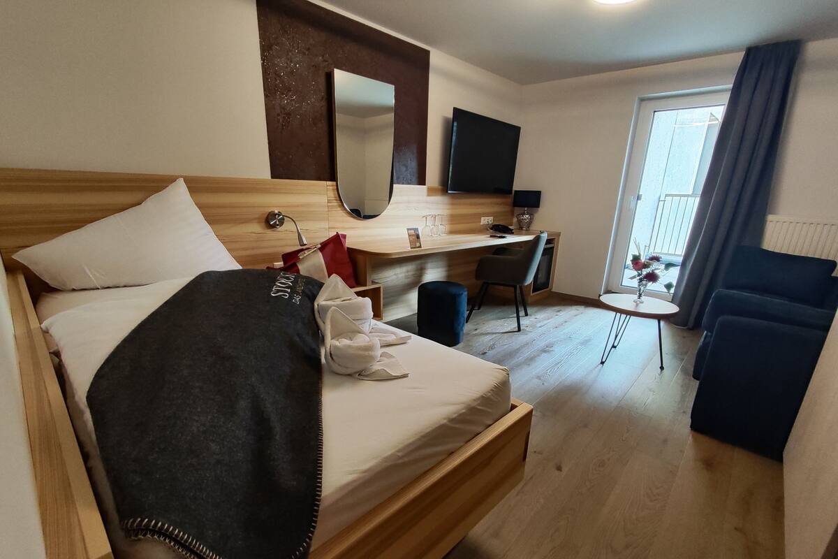 Hotellihuone, jossa on sänky, työpöytä, tuoli, televisio ja ikkuna, jossa on verhot.