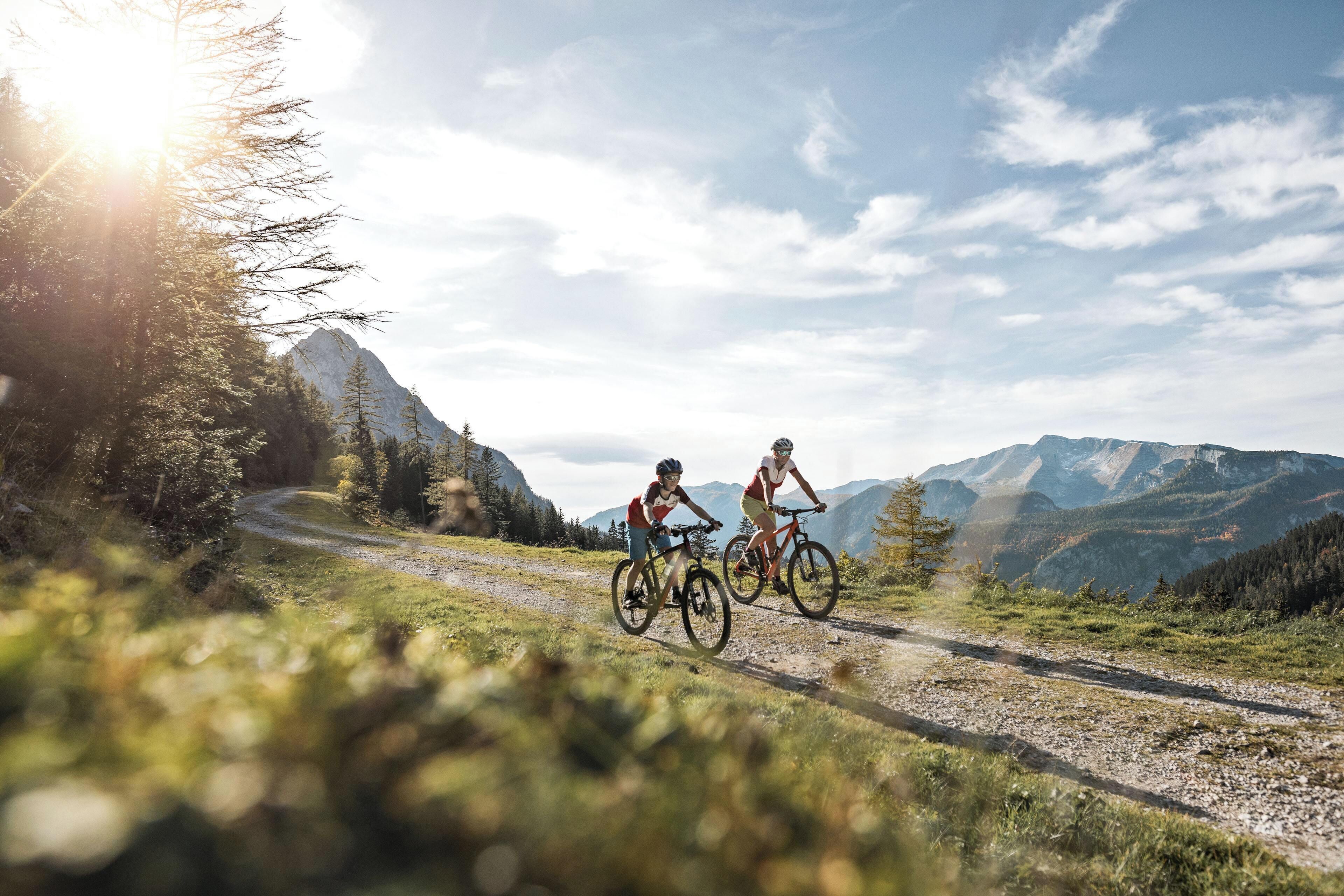 Two cyclists on a gravel path with mountains in the background.