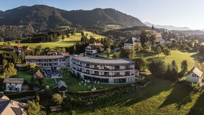 A multi-story hotel with a circular design, surrounded by lush greenery and a mountainous backdrop. - Landhotel das Stocker (Vorderstoder)