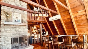 An attic room with a stone fireplace, wooden beams, and a dining area with chairs.