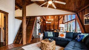 A spacious loft with a large wooden staircase, a dark blue sectional sofa, and a stone fireplace.
