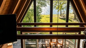 A room with a large window, wooden beams, a view of a grassy area, and a table with candles.