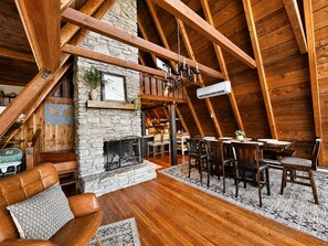 Acogedor loft con chimenea de piedra, vigas de madera y zona de comedor con sillas y mesa.
