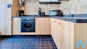 A modern kitchen with wooden cabinets, a black oven, a coffee machine, and a microwave. - Cosy Sunny Apartment Near Zeedijk (Knokke-Heist)
