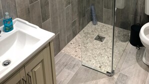 Moderni kylpyhuone, jossa on lasiseinällä varustettu suihku, valkoinen pesuallas ja wc.