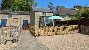 Une charmante maison en pierre avec un toit de chaume, une clôture en bois et un chemin de gravier menant à une terrasse en bois.