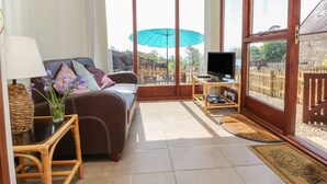 Un salon confortable avec un canapé, un téléviseur et une grande fenêtre donnant sur un jardin.