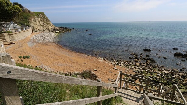 Une plage côtière avec un escalier en bois qui descend jusqu'au rivage.