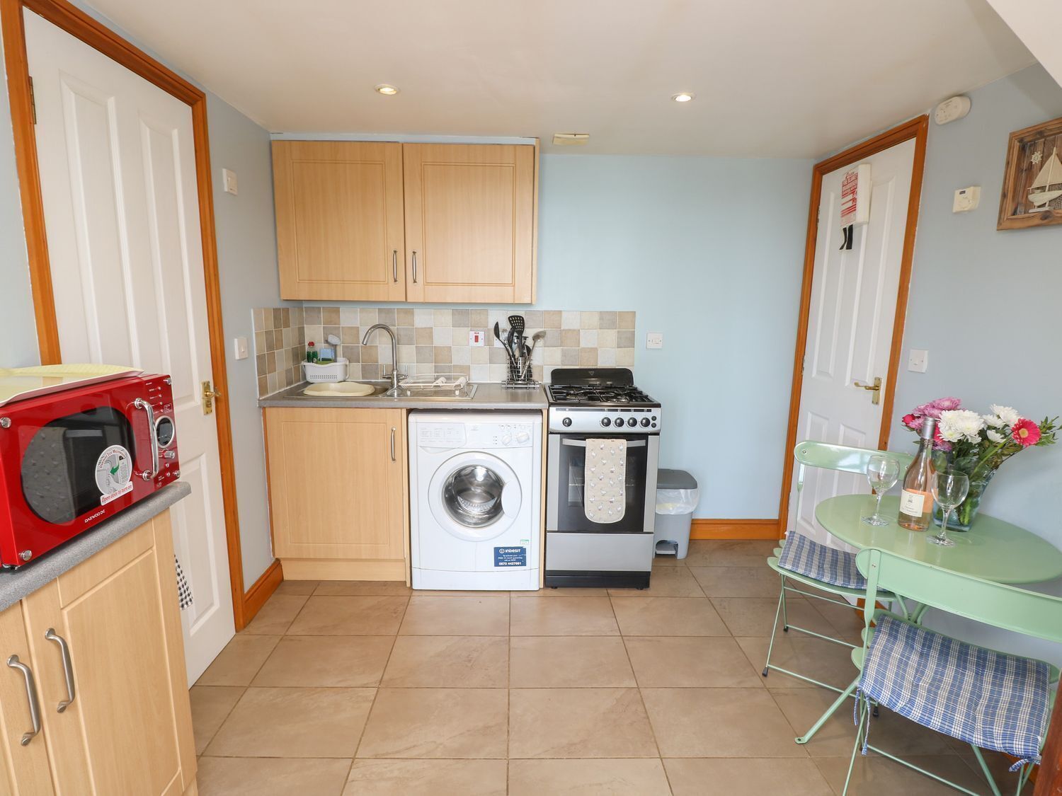 Une cuisine compacte avec des meubles en bois, un lave-linge, une cuisinière et une petite table à manger avec des chaises.