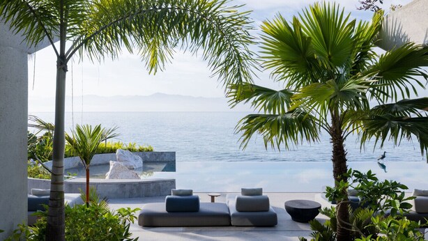 Un espacio moderno al aire libre con vistas al mar, que incluye un banco de piedra y sillones de descanso.
