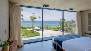 Un dormitorio con un gran ventanal corredera que da a un balcón con vista al océano.