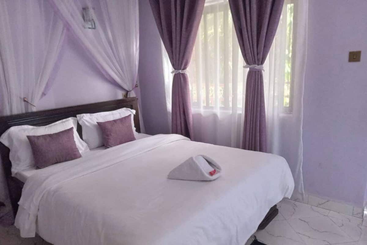A neatly made bed with white and purple bedding, a bedside table with a white phone, and purple curtains.