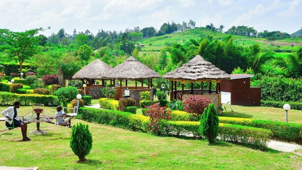 A lush garden with thatched-roof gazebos, manicured hedges, and a small pond. - Rosa Gardens Hotel (Muhoroni)
