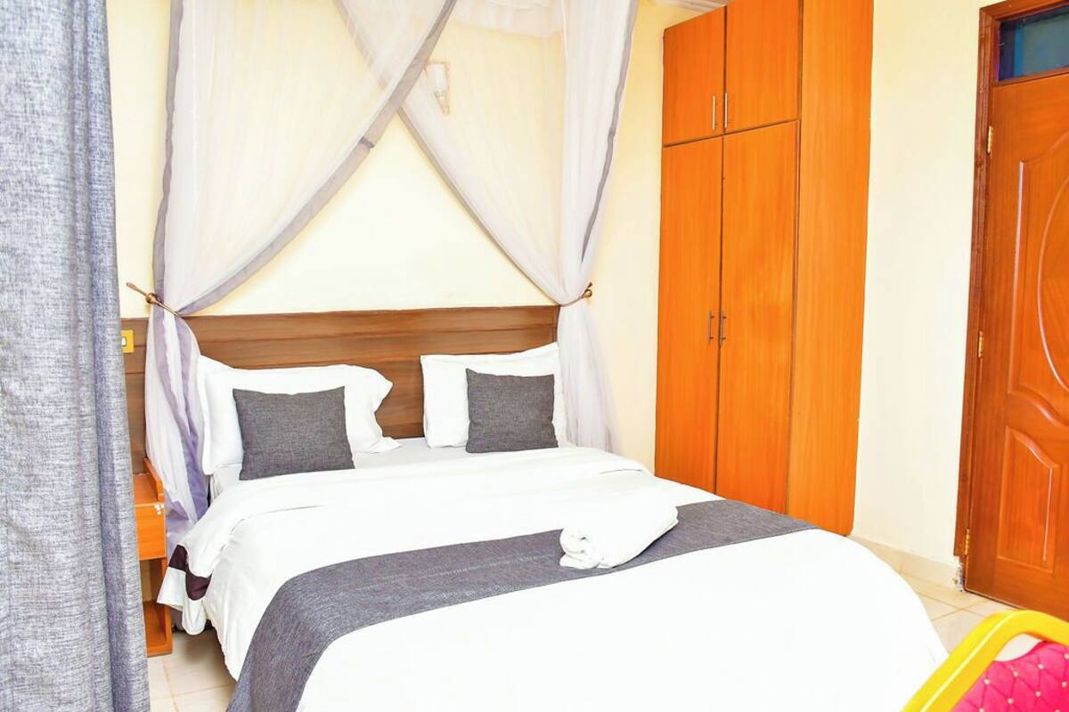 A neatly made bed with white and gray bedding, a wooden headboard, and a mosquito net.