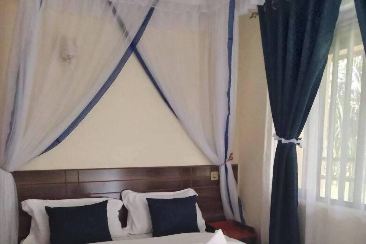 A neatly made bed with a white and navy blue bedspread, a white pillow, and a navy blue pillow. There is a wooden headboard, a nightstand with a lamp, and a window with blue curtains.