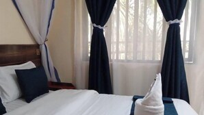 A neatly made bed with white and blue bedding, a white towel, and a blue blanket. - Rosa Gardens Hotel (Muhoroni)