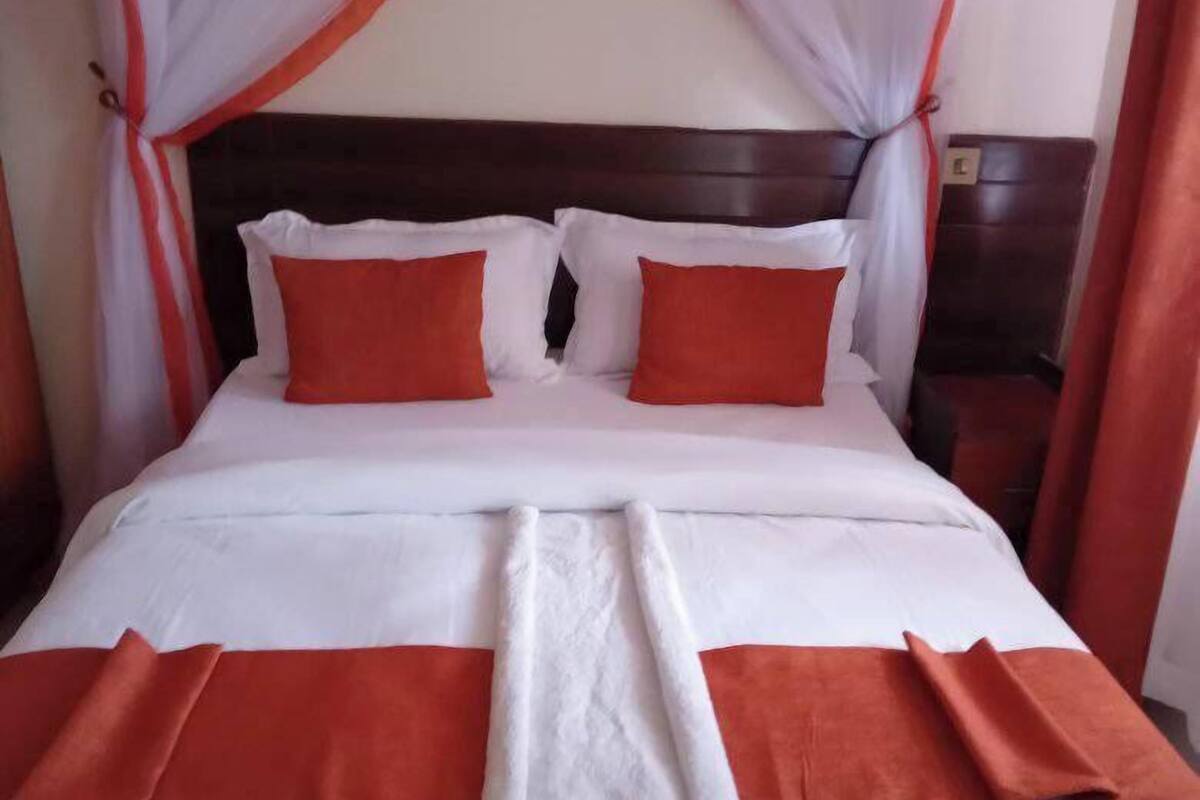 A neatly made bed with white and orange bedding, a wooden headboard, and a nightstand with a lamp.