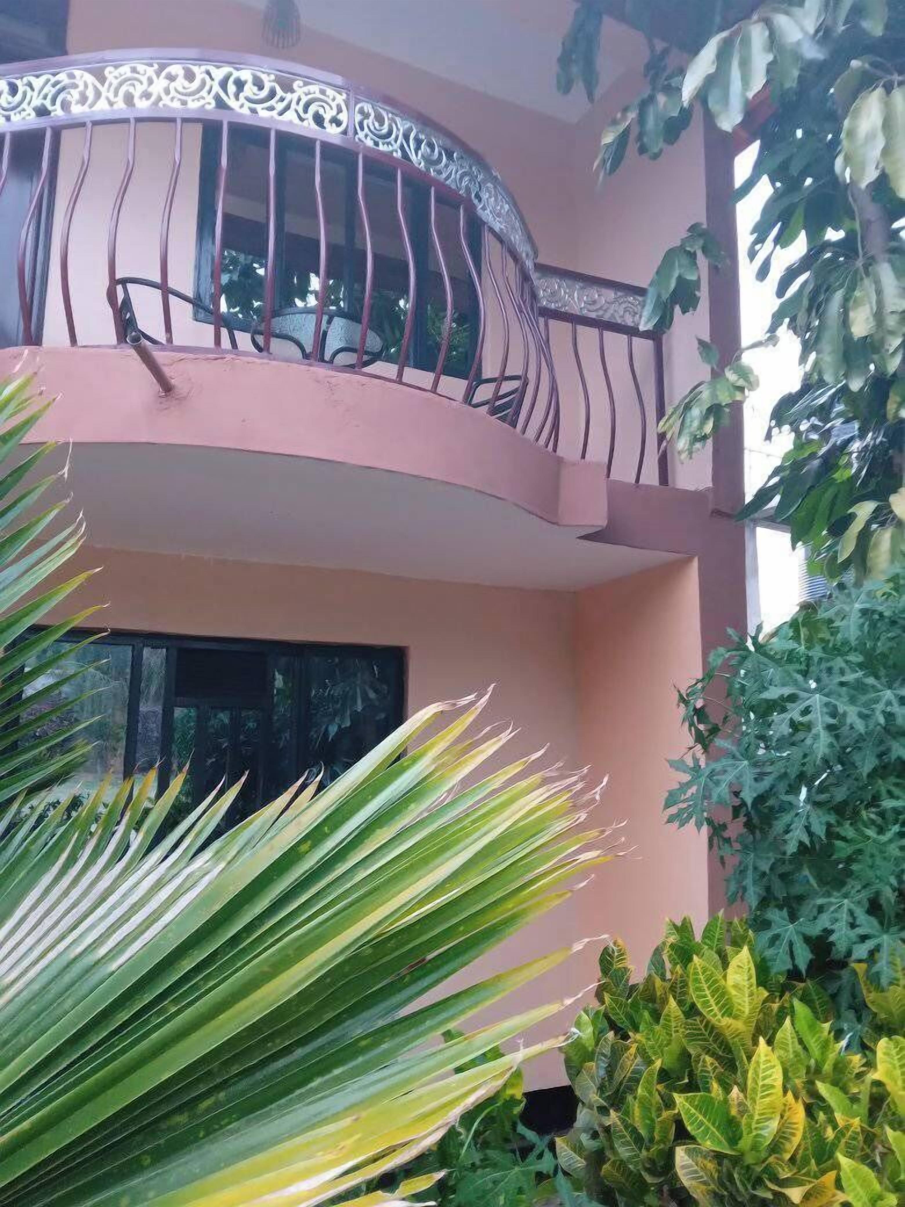 Un edificio rosa con un balcone, circondato da piante verdi.