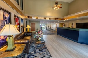 A spacious lobby with a leather sofa, a coffee table with a vase of flowers, a reception desk, and a ceiling fan.