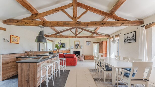 Une cuisine spacieuse avec un îlot central en bois, un coin repas avec une table et des chaises, et un salon avec un canapé et une cheminée.