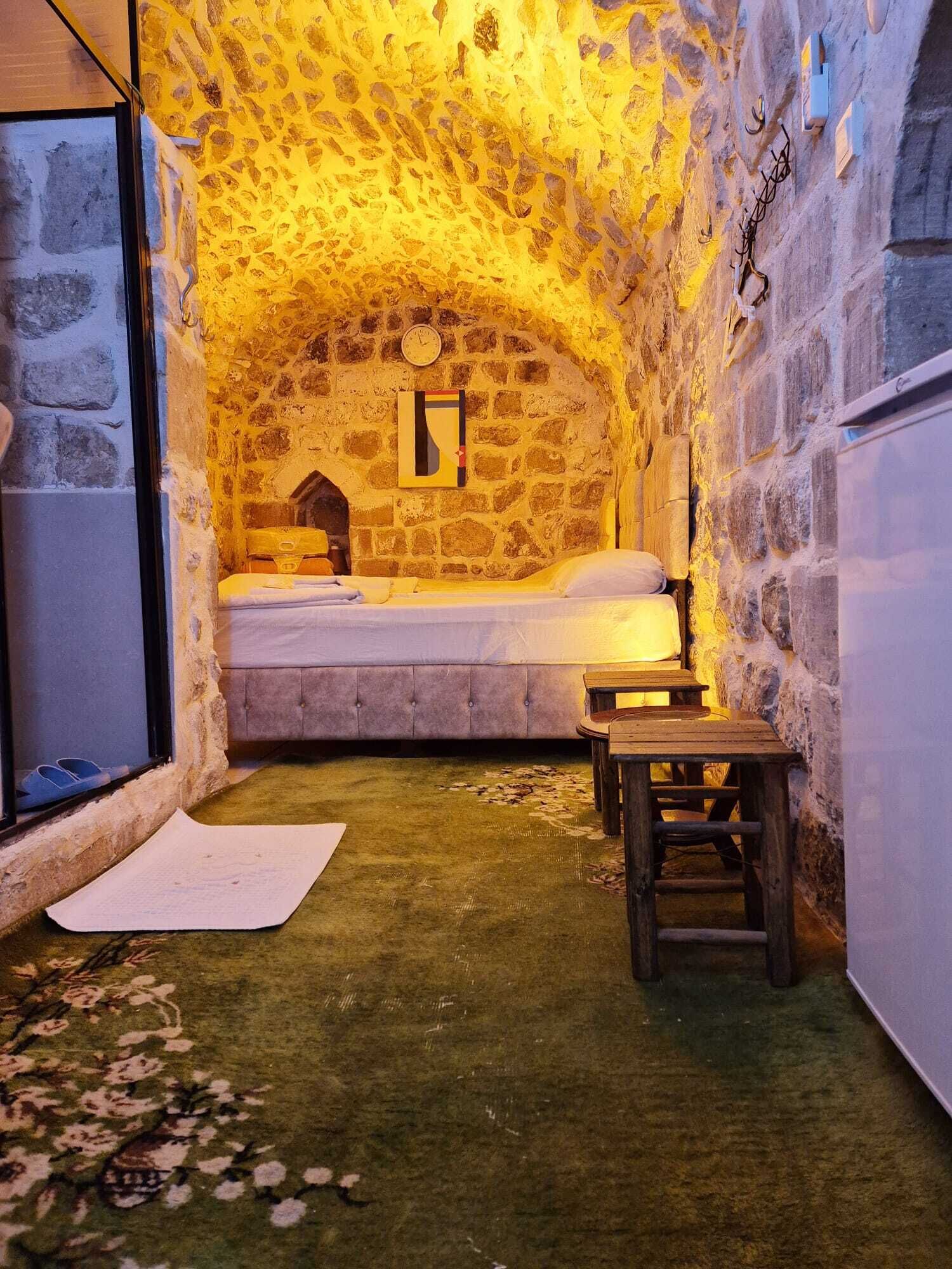 A cozy room with a stone wall, a bed, a wooden bench, and a small table.