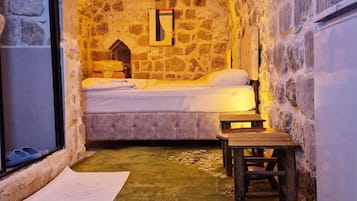 A cozy room with a stone wall, a bed, a wooden bench, and a small table.