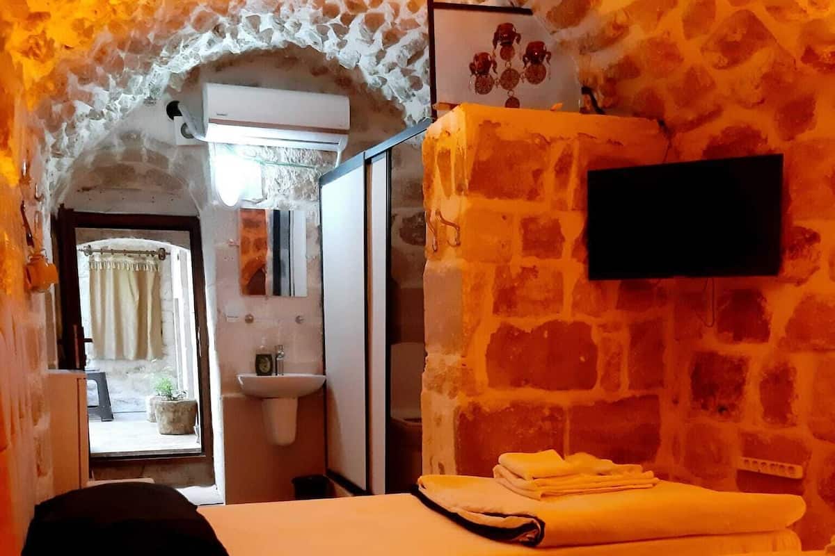 A room with a stone wall, a bed with a folded towel, a small table, and a mounted television.