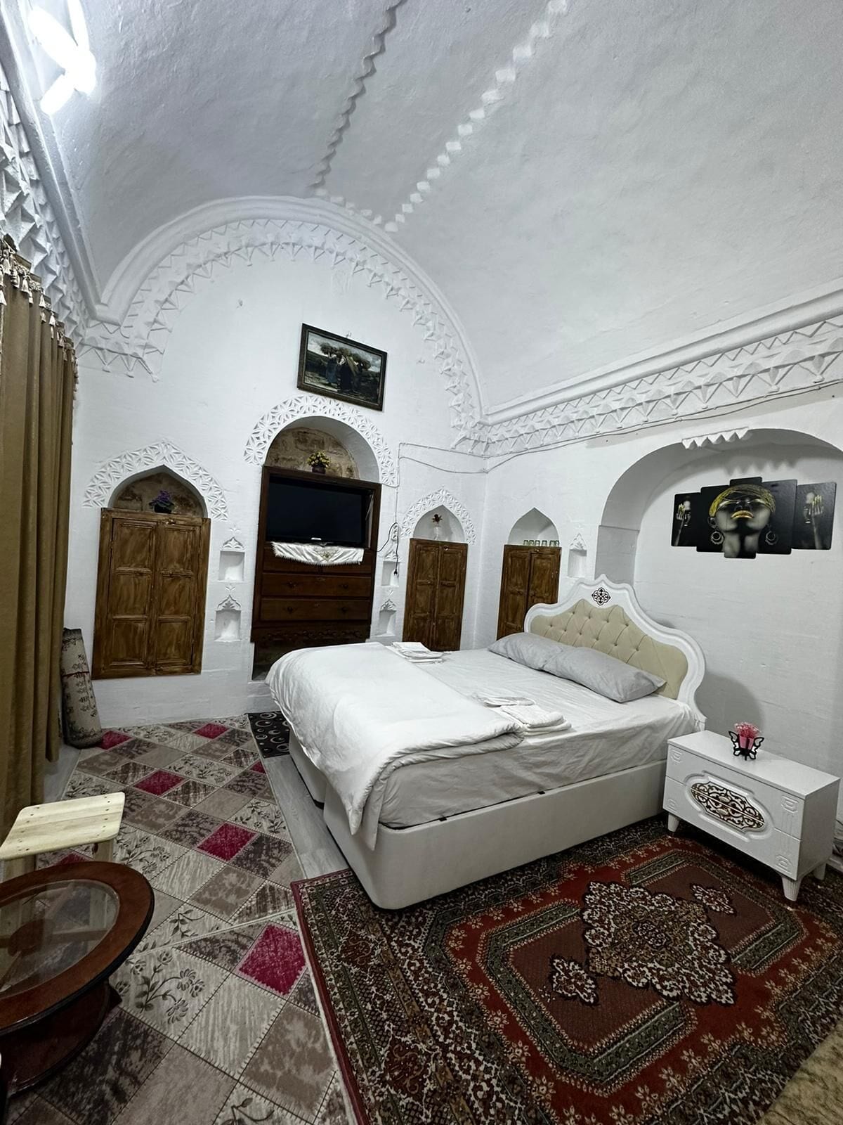 Un dormitorio con cama, mesita de noche y alfombras decorativas.