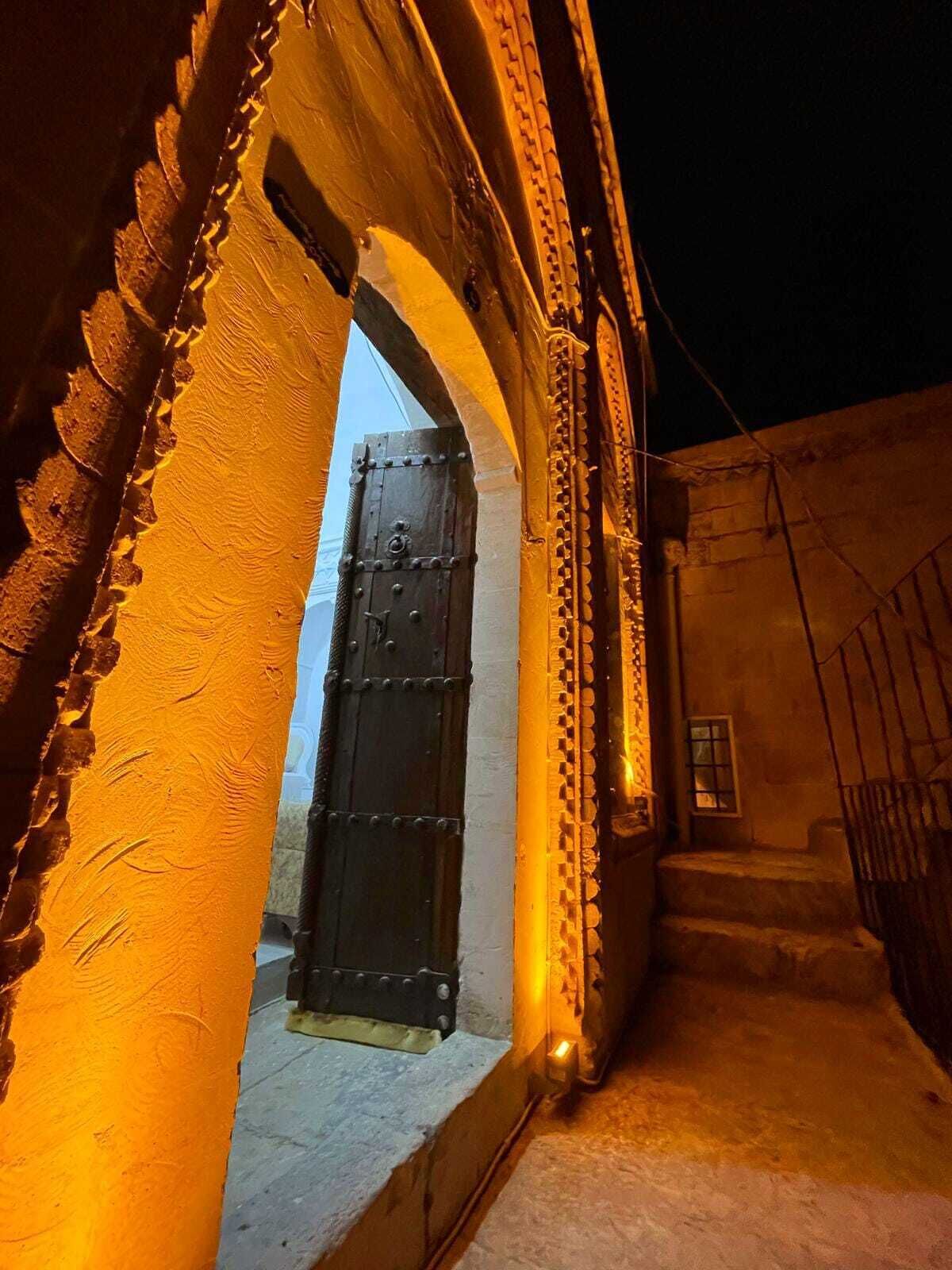 An arched doorway leading to a dimly lit interior space with a metal gate and a staircase.